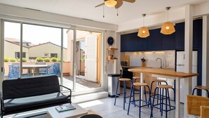 A modern kitchen with a bar area, a dining area with a sofa and table, and a sliding glass door leading to an outdoor patio. - Apartment 'Notre Dame' with Sea View, Private Terrace and Wi-Fi (Capbreton)