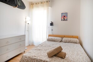 A bedroom with a bed, a dresser, a lamp, a poster, and a curtain. - Apartment 'Notre Dame' with Sea View, Private Terrace and Wi-Fi (Capbreton)