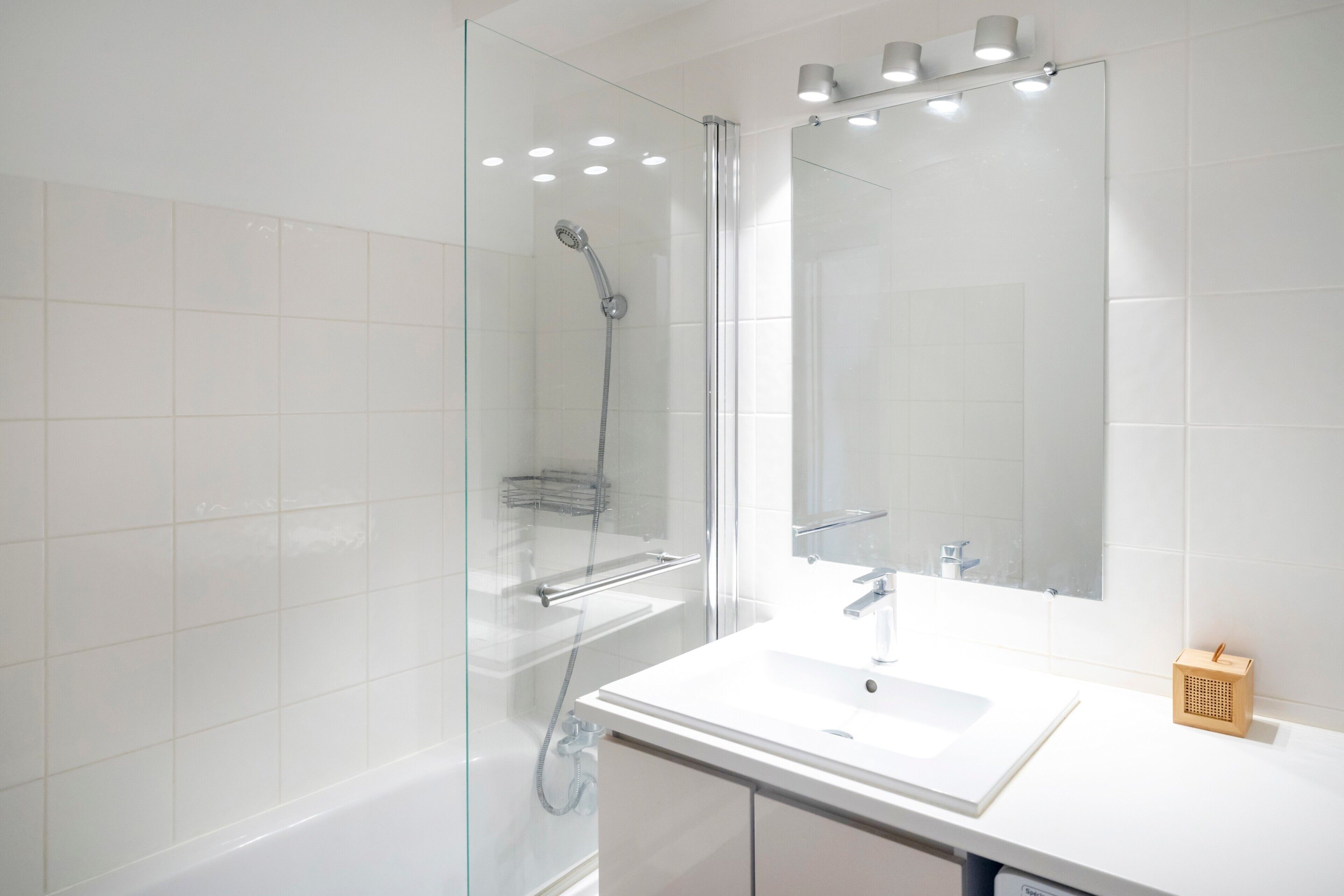 Un baño moderno con ducha envuelta en vidrio, un lavabo blanco y un espejo grande.