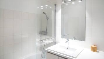 Un baño moderno con ducha envuelta en vidrio, un lavabo blanco y un espejo grande.