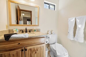 Un baño con tocador de madera, un espejo grande, un inodoro y un perchero con toallas.