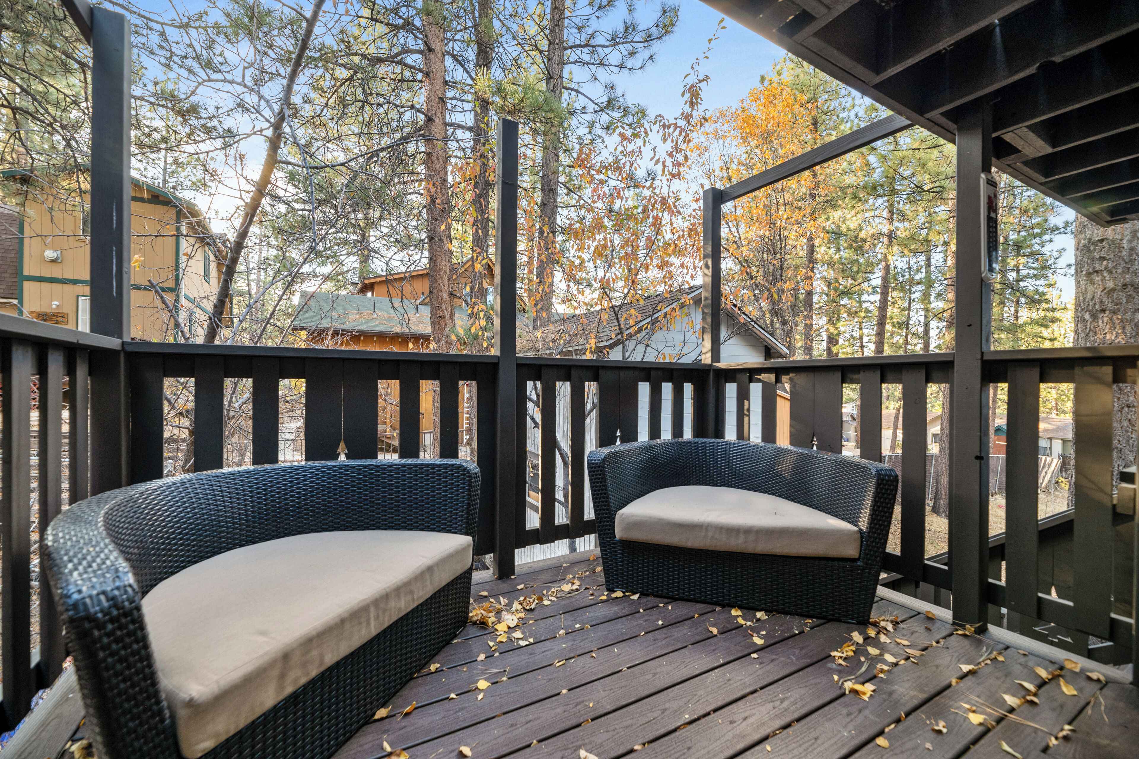 Eine Holzterrasse mit zwei Korbstühlen und einer Bank, umgeben von Bäumen und Gebäuden.
