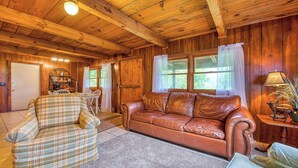 Ein gemütliches Blockhaus-Interieur mit einer braunen Ledersofa, einem karierten Sessel und einer Essecke mit Holztisch und Stühlen.