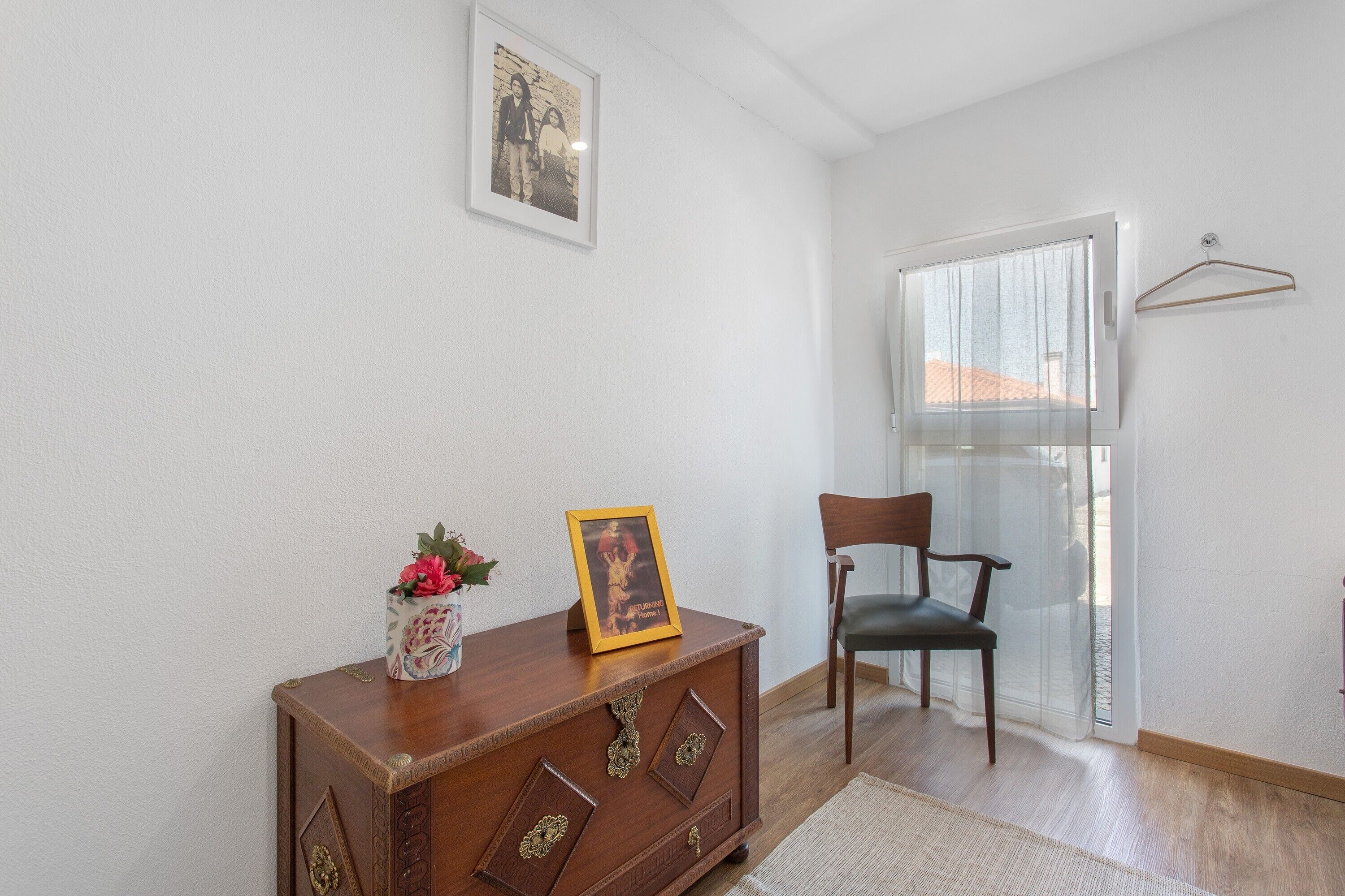 A room with a wooden cabinet, a chair, a framed picture, and a window with a curtain.