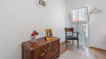 A room with a wooden cabinet, a chair, a framed picture, and a window with a curtain.