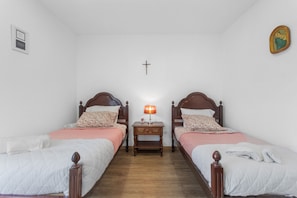 A room with two beds, a nightstand, a cross on the wall, and a framed picture. - Room 'Santo Agostinho' with Shared Terrace, Shared Garden and Wi-Fi (Fátima)