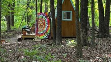 A wooden cabin in a forest with a colorful circular artwork on a bench.