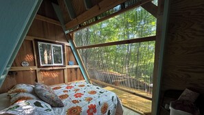 A cozy bedroom with a bed, a window, and a chair. - Charming A-frame cabin set in the woods overlooking deep wooded ravines. (Charleston)