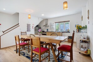 A dining area with a wooden table and chairs, a kitchen in the background, and a staircase.