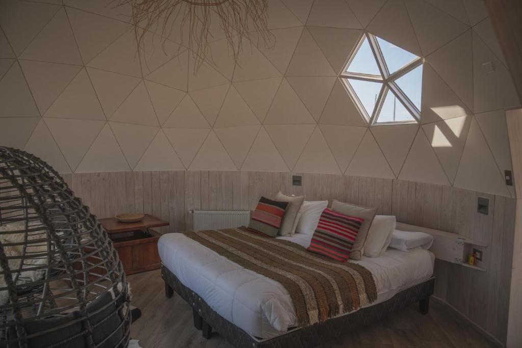 Camera da letto con un design geometrico del soffitto, un letto con molti cuscini, un comodino in legno e una sedia in vimini.