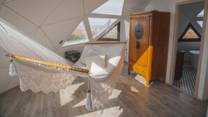 Un hamac dans une pièce dotée de lucarnes, d’une armoire en bois et offrant une vue sur l’extérieur.