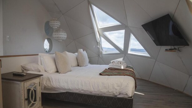 Une chambre à coucher comprenant un lit, une table de chevet, un téléviseur et une grande fenêtre de toit.