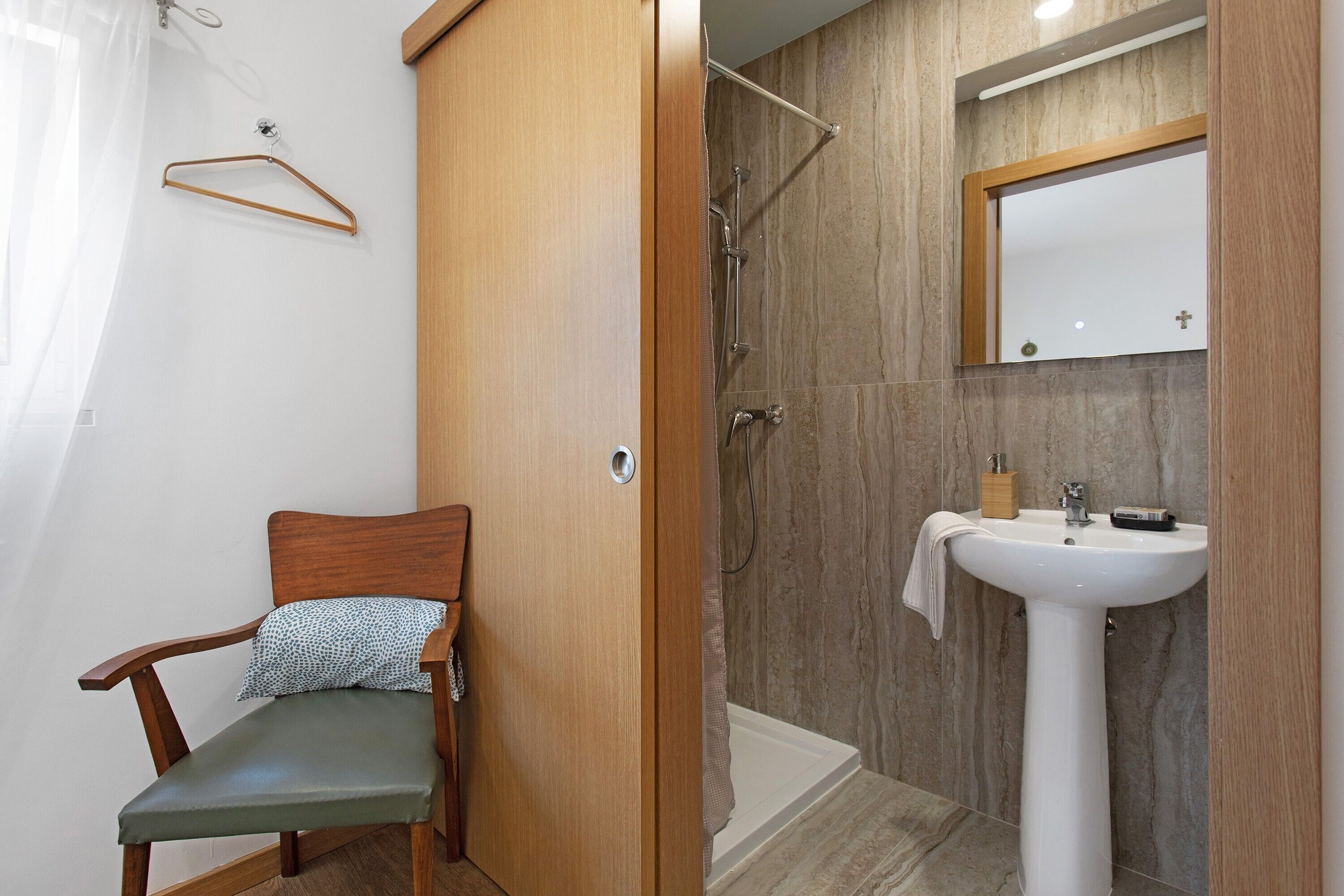 Un bagno con una sedia di legno, una doccia, un lavandino e uno specchio.