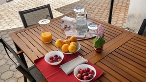 Une table en bois avec un set de table rouge, des corbeilles de fruits, un pichet en verre et un vase rempli de fleurs.