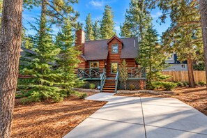 A log cabin with a wooden deck, a chimney, and a fenced yard surrounded by pine trees. - Fox Cabin (Big Bear City)