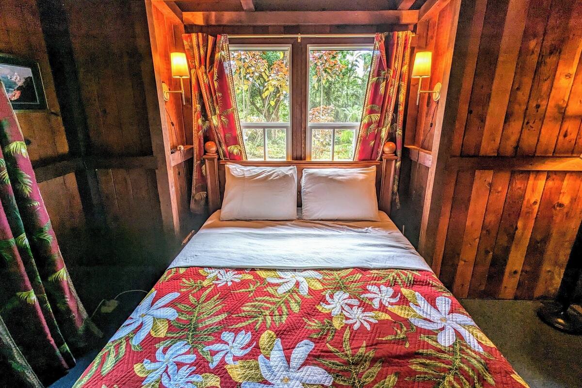 A wooden room with a bed, curtains, and a window.