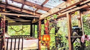 A wooden deck with a bed, string lights, and hanging plants.