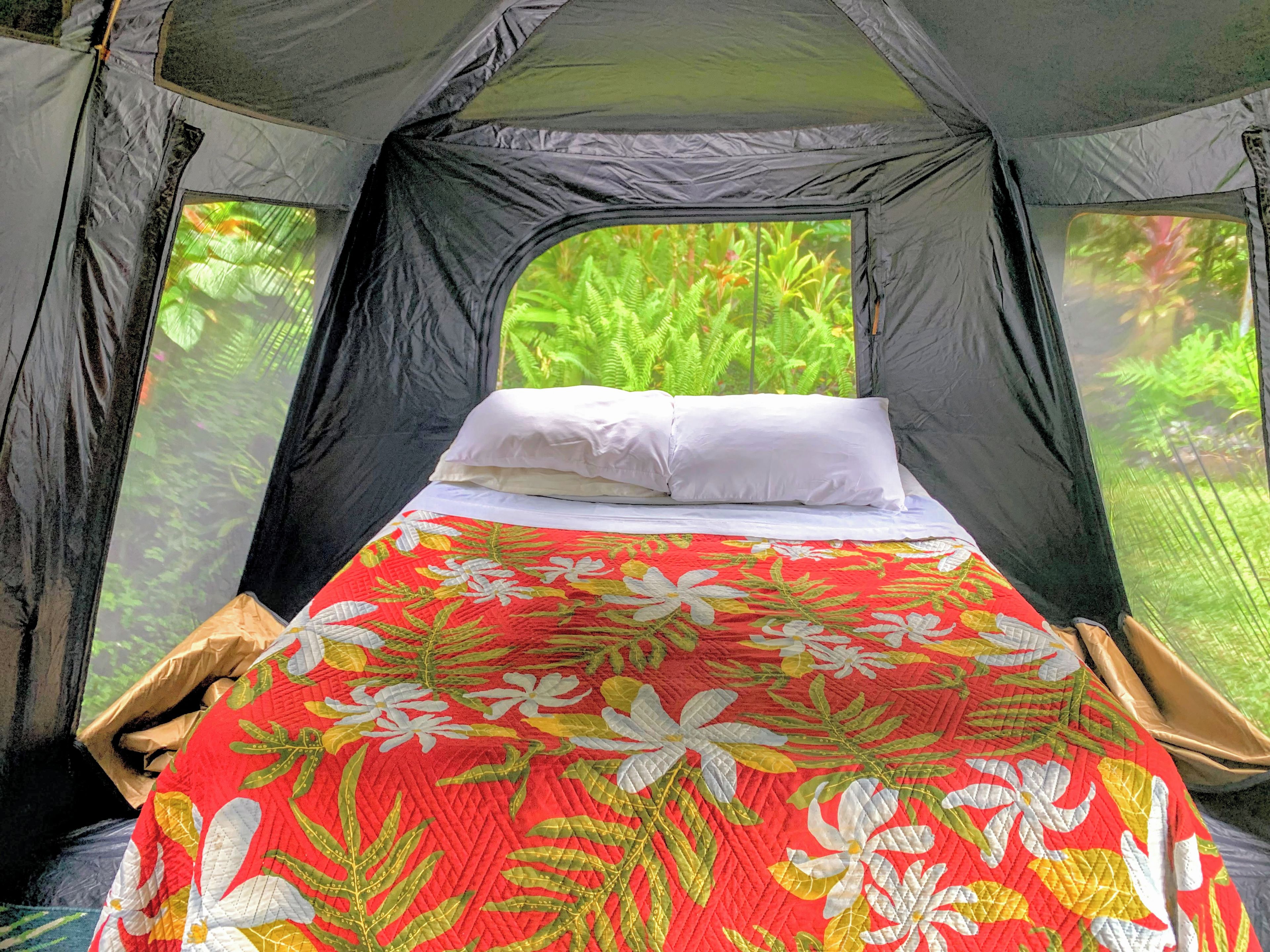 A tent with a bed, white pillows, and a floral-patterned bedspread.