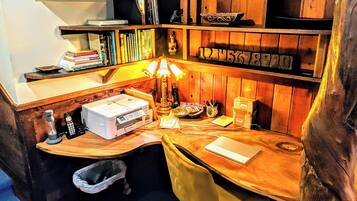 Un espace de travail accueillant, avec un bureau en bois, une lampe, une imprimante et une bibliothèque remplie de livres et d’objets décoratifs.