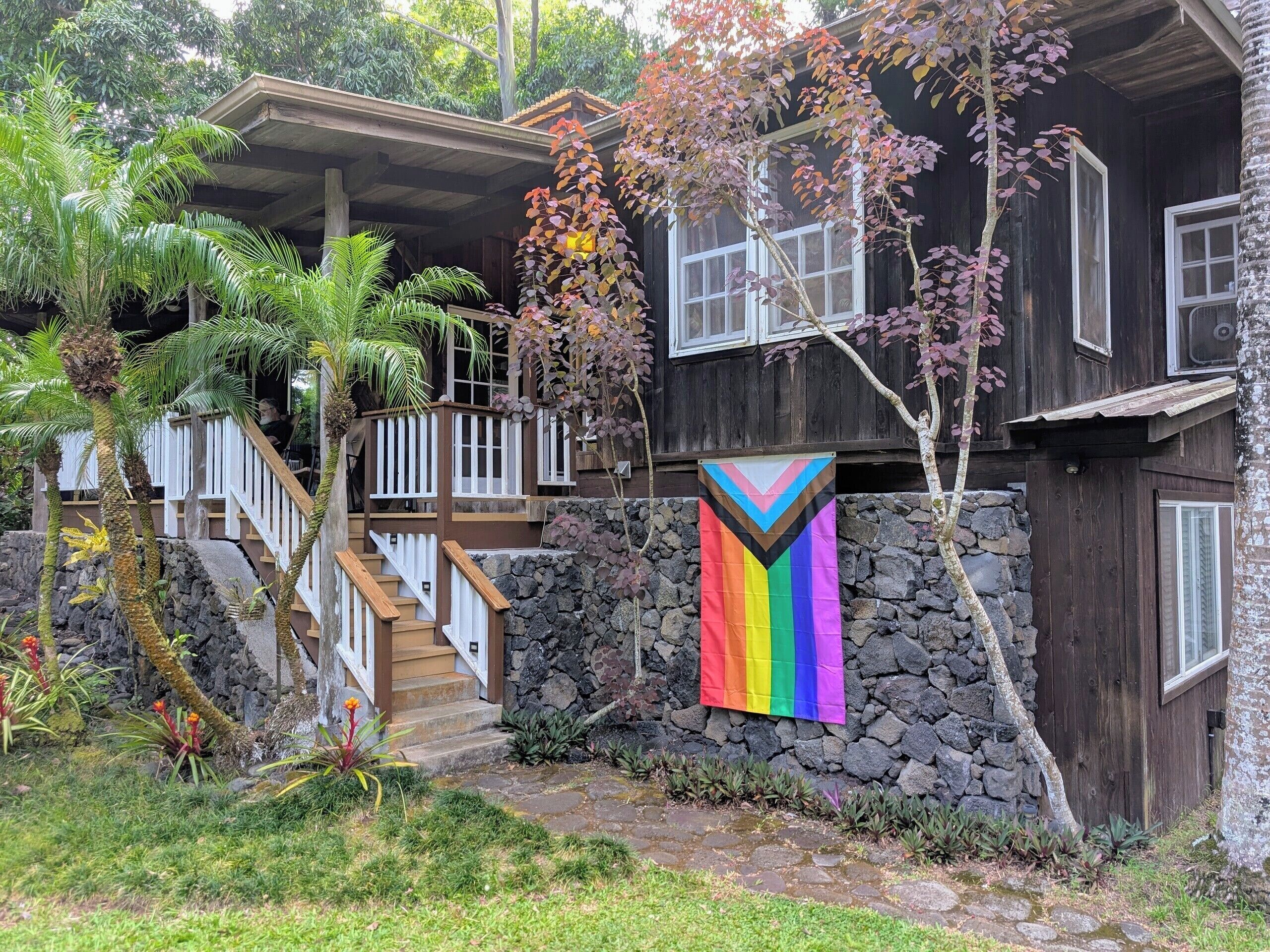 A wooden house with a stone wall, a staircase, and a rainbow flag.