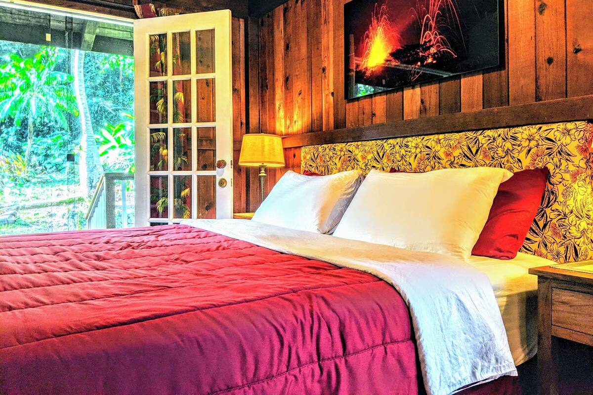 A bed with a red quilt, white pillows, and a wooden headboard with a floral pattern.