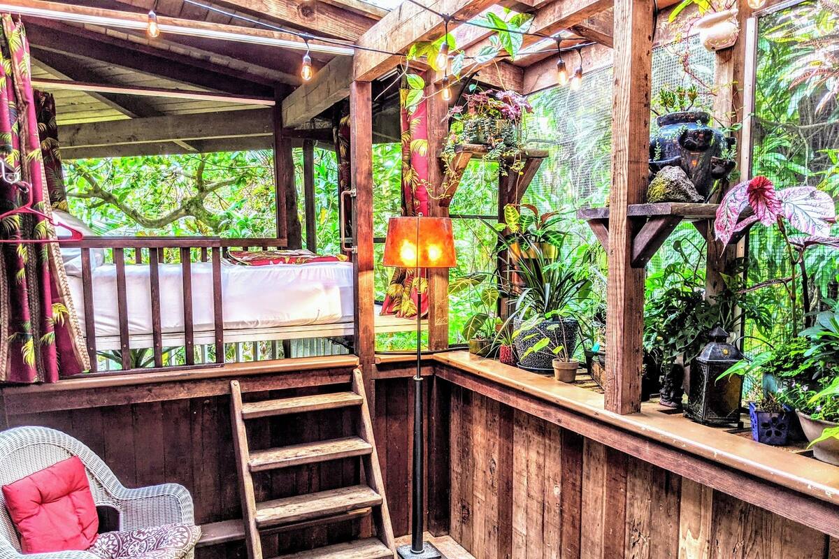 A wooden deck with a ladder, a wicker chair, and a table with a red cushion.
