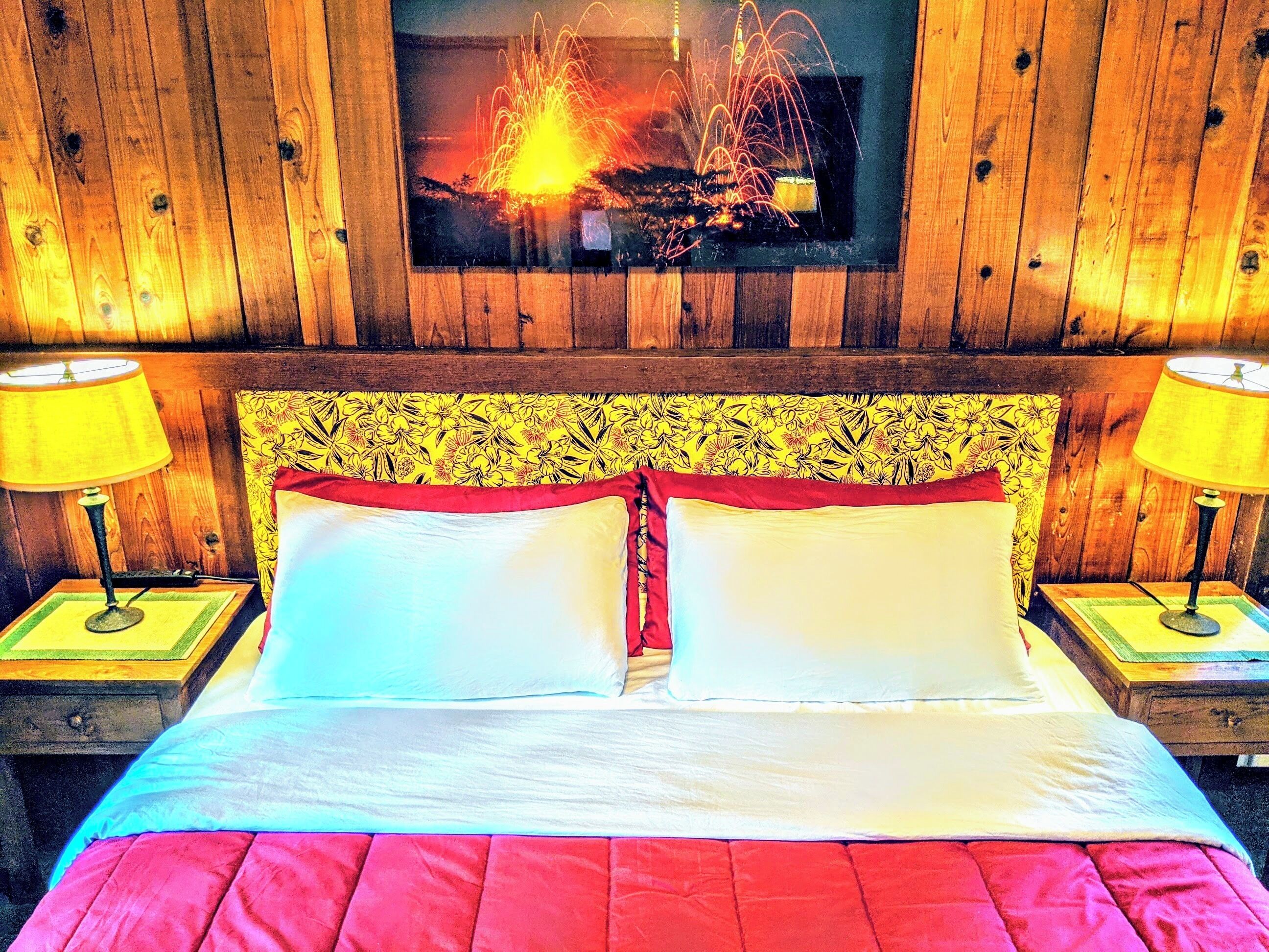 A bed with two pillows, a wooden headboard, and a television above it.