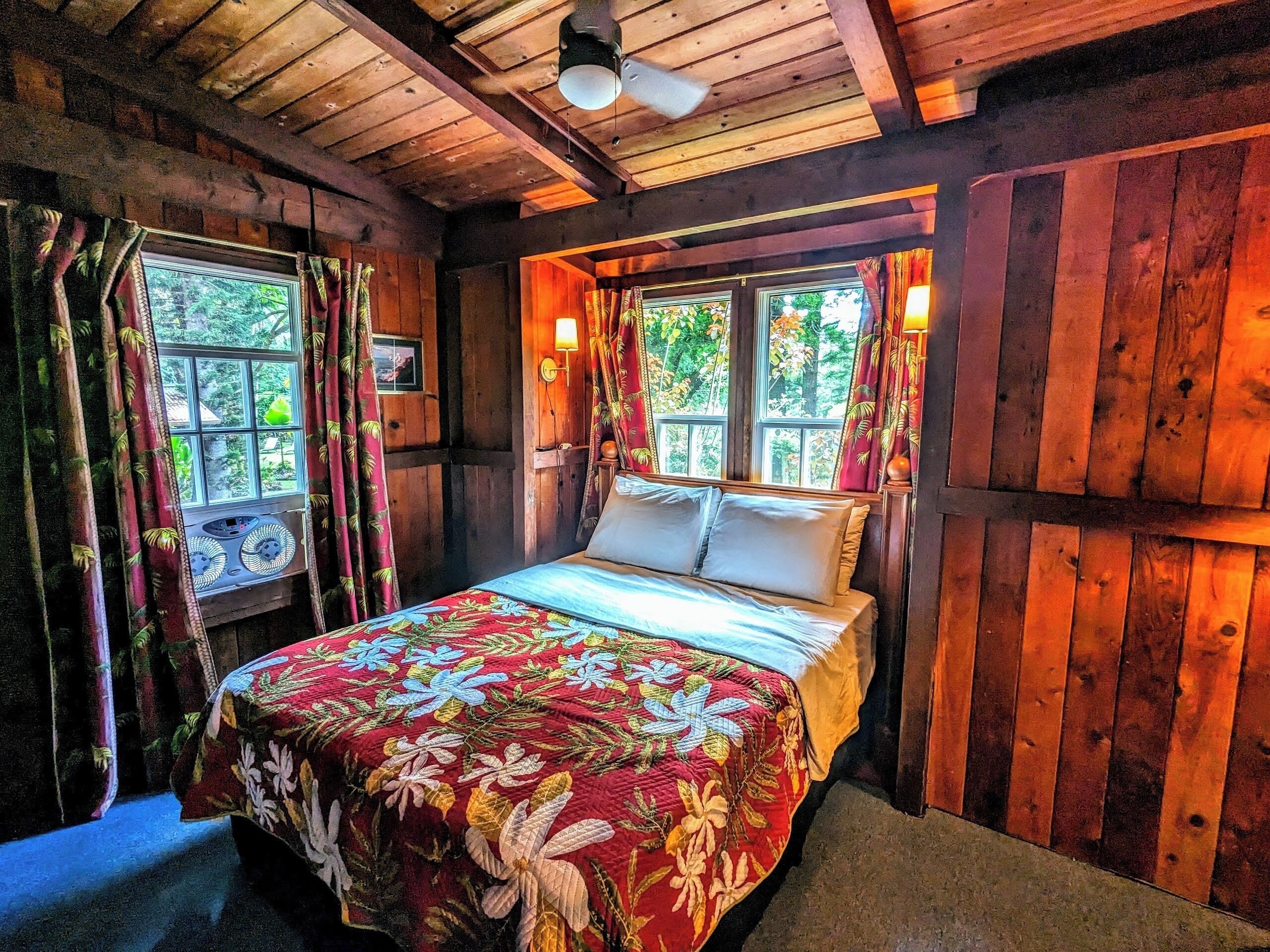Une chambre dans une cabane en bois, avec un lit, des rideaux et une fenêtre donnant sur un paysage verdoyant.