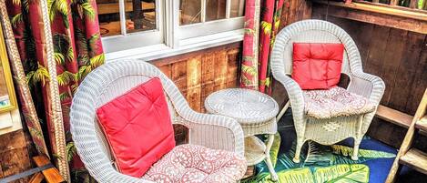 A cozy seating area with wicker chairs and a small round table, featuring tropical-themed curtains and a patterned rug.