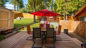 A wooden deck with a table and chairs, a red umbrella, and a wooden fence. - Mama Bear's Cottage (Big Bear Lake)