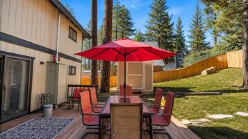 A deck with a table and chairs, a red umbrella, and a wooden fence.