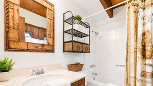 A bathroom with a wooden vanity, a sink, a toilet, a shower, and a mirror with a rustic frame. - Mama Bear's Cottage (Big Bear Lake)