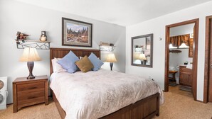 A bedroom with a wooden bed, two bedside tables with lamps, a wall-mounted picture, and a mirror. - Mama Bear's Cottage (Big Bear Lake)