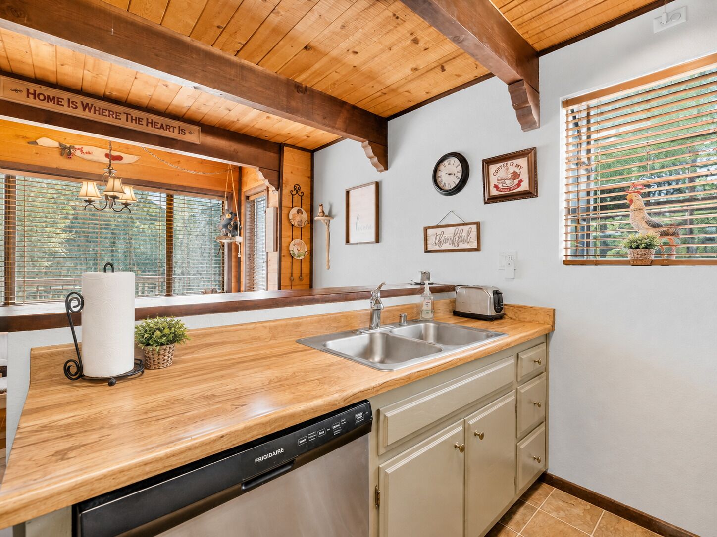 A kitchen with wooden beams, a dishwasher, a sink, and a window with blinds.