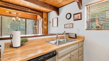 A kitchen with wooden beams, a dishwasher, a sink, and a window with blinds.