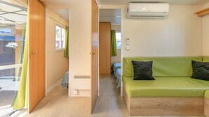 Une pièce avec un canapé vert, un appareil de climatisation et une porte coulissante donnant sur une autre pièce.