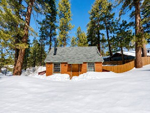 A cabin surrounded by snow with a wooden fence and tall pine trees. - Highland Hideaway (Big Bear Lake)