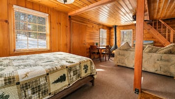 A log cabin interior with a bed, a sofa, a dining table, and a fireplace.