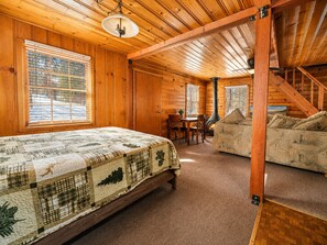 A log cabin interior with a bed, a sofa, a dining table, and a fireplace. - Highland Hideaway (Big Bear Lake)