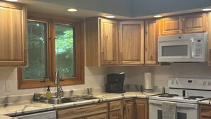 Una cocina con armarios de madera, encimera de mármol blanco, microondas integrado, cafetera y estufa.