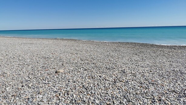 Une plage de galets, avec un ciel bleu clair et une mer calme.