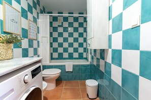 A bathroom with a checkered tile pattern, a toilet, a washing machine, and a bathtub. - Global Vacacional: Ground floor with pool in Almenara (Almenara)