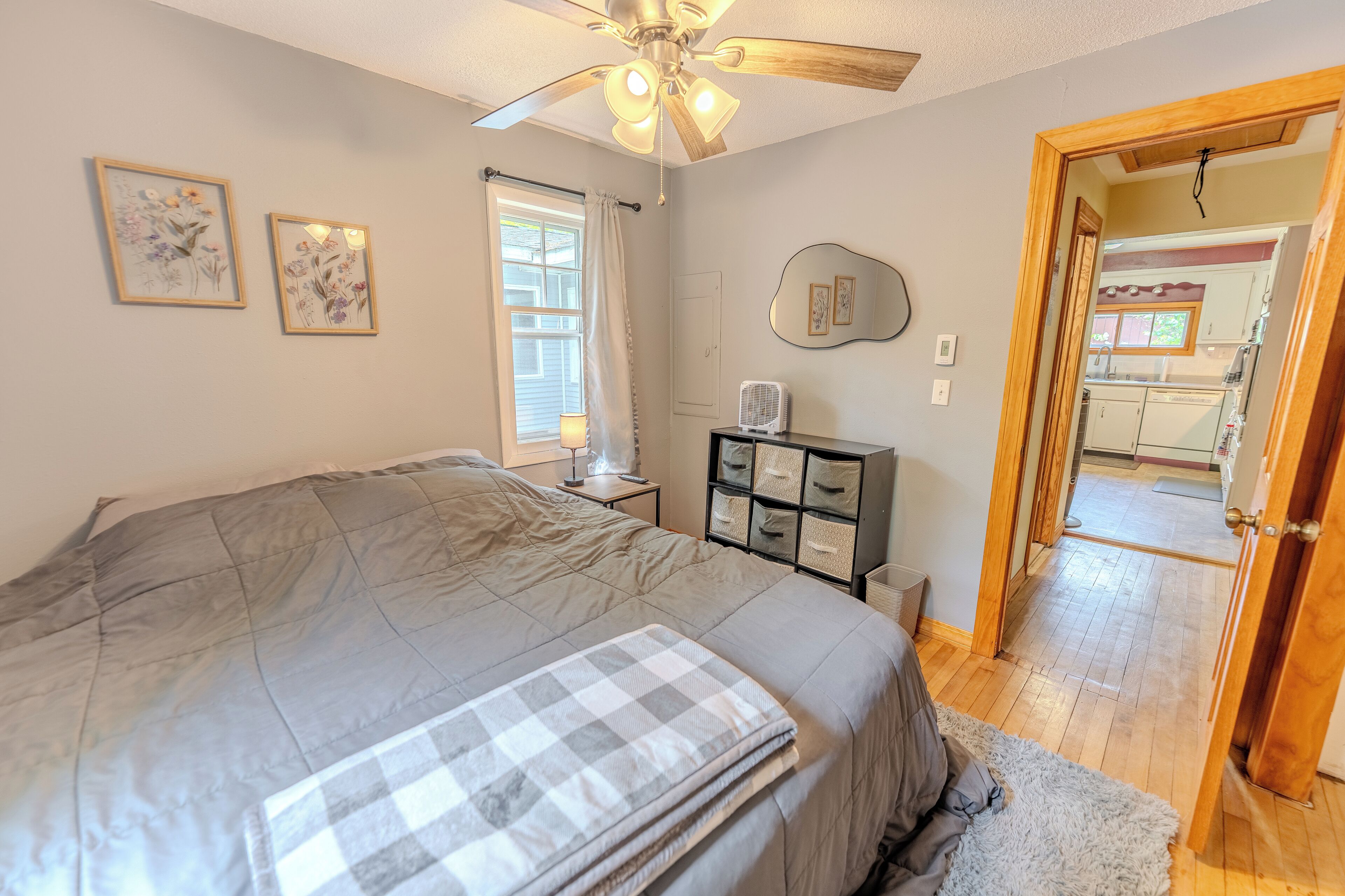 Une chambre avec un grand lit, un ventilateur de plafond, une table de chevet, une commode et une porte donnant sur la cuisine.