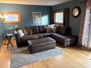 A living room with a sectional sofa, a small side table, a floor lamp, a rug, and a wall clock.