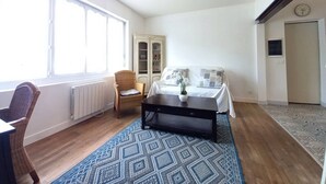 A bedroom with a bed, a chair, a coffee table, a window, a radiator, a wardrobe, and a door.