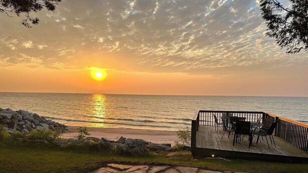 A sunset view from a deck overlooking the ocean, with a fire pit and outdoor seating. - Hot Tub | Sleeps 20 | Private Beach | Game Room (Two Rivers)
