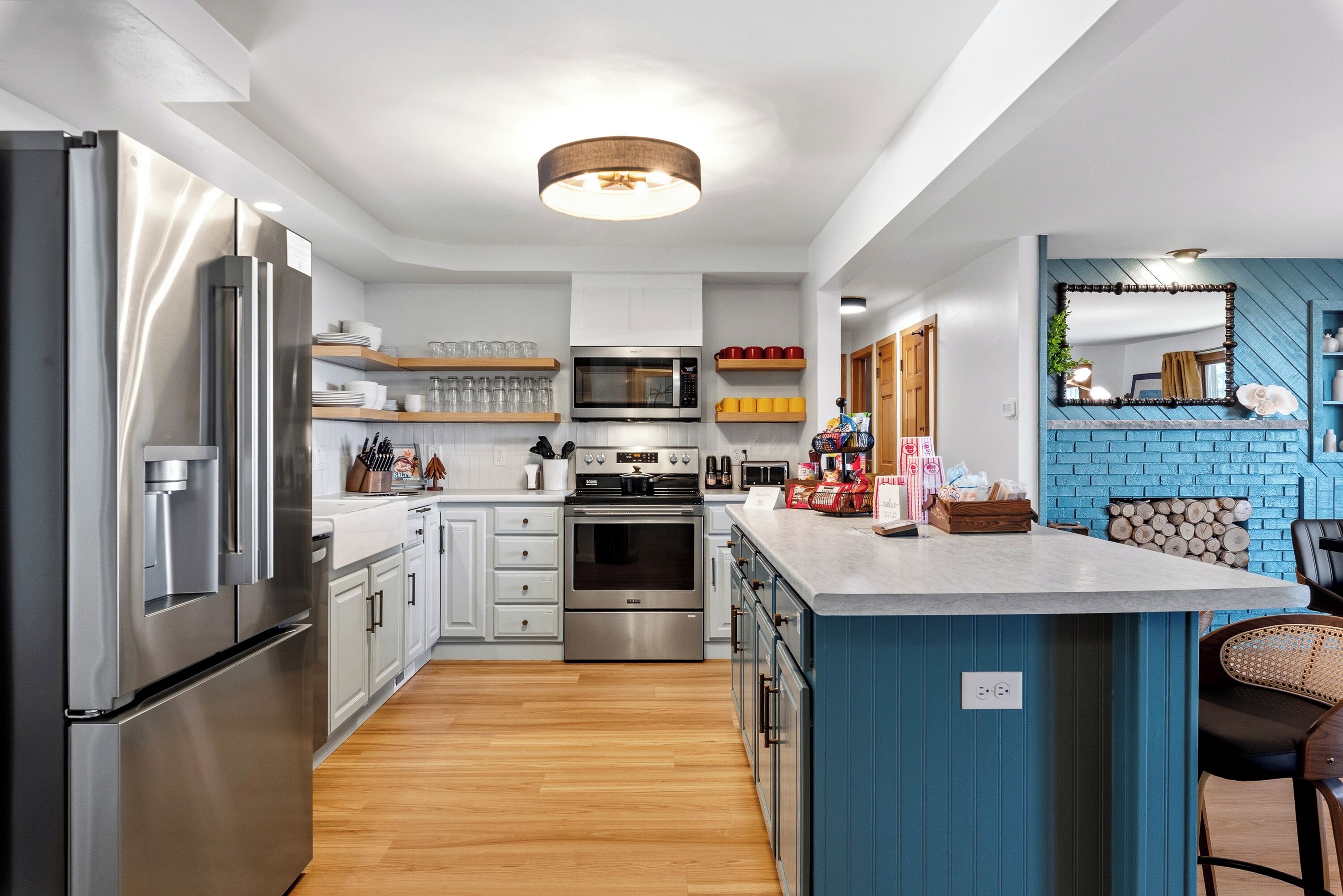 A modern kitchen with stainless steel appliances, wooden flooring, and a blue accent wall.