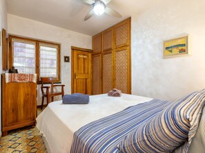 A bedroom with a bed, a desk, a chair, a wardrobe, and a ceiling fan. - Lu Nibbaru di Portobello by Interhome (Portobello)