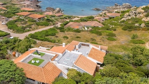 A coastal residential area with houses featuring red-tiled roofs, surrounded by greenery and rocky terrain. - Lu Nibbaru di Portobello by Interhome (Portobello)