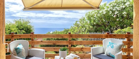 An outdoor patio with wicker furniture, a table with drinks, and a view of the sea.